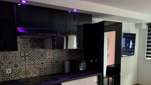 A modern kitchen with a black refrigerator, a microwave, and a built-in oven. There is a patterned rug on the floor and a television mounted on the wall. - Le Mini Versailles (Goussainville)