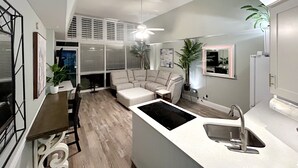 Una cocina moderna con isla integrada, un comedor con mesa y sillas, y una sala de estar con sofá y ventilador de techo.