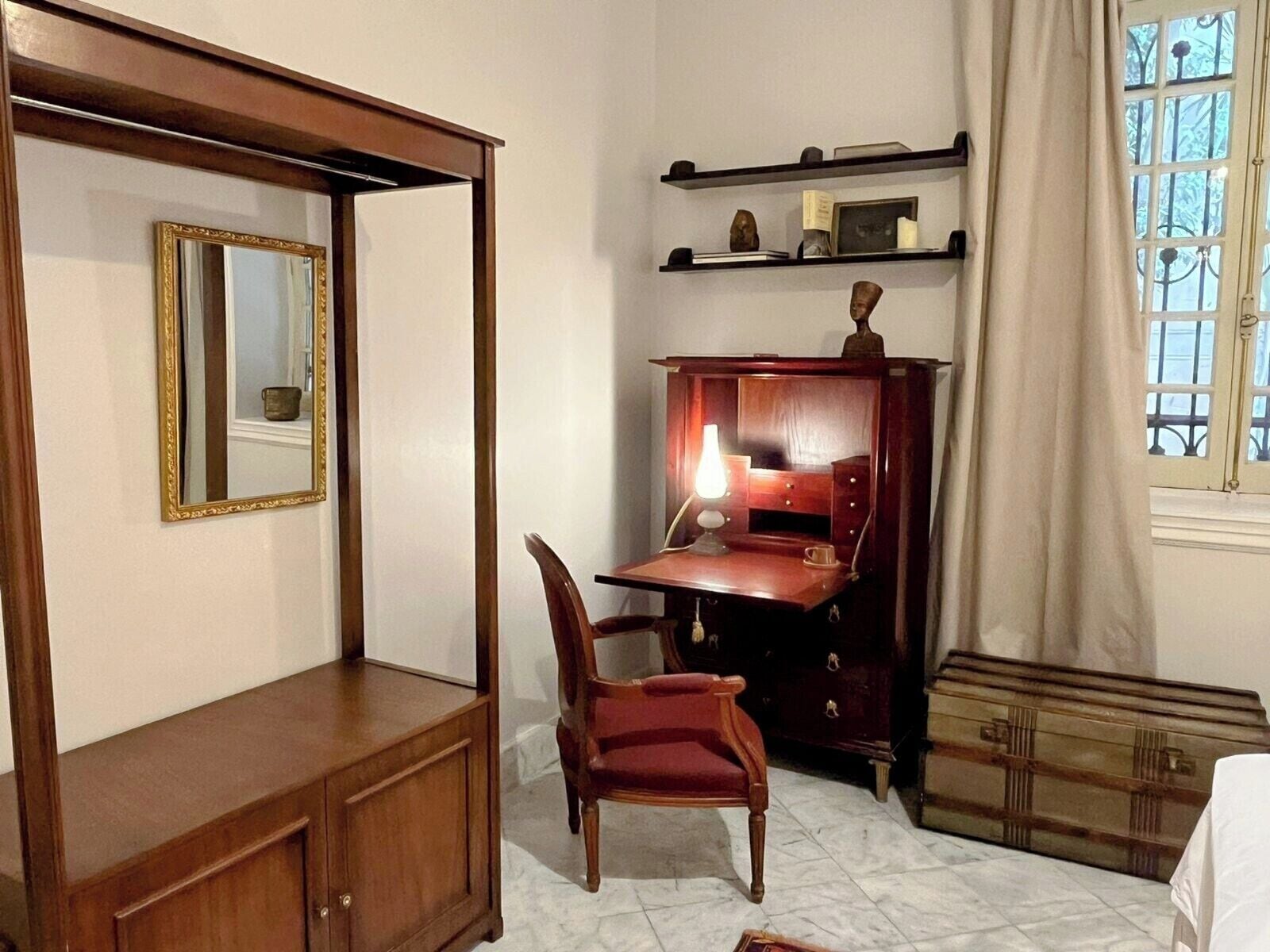 Une chambre à coucher avec un lit à baldaquin, un bureau en bois avec une chaise, un miroir et une fenêtre avec des rideaux.