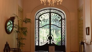 A room with a chandelier, a large window with intricate ironwork, a wooden bench, and a patterned rug.