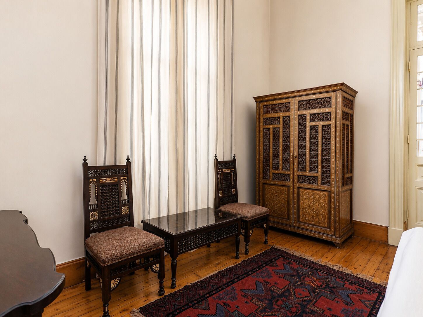Una habitación con un armario de madera, dos sillas, una mesa y una alfombra estampada.