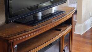 Een flatscreen televisie op een houten entertainment meubel met een glazen kast eronder.