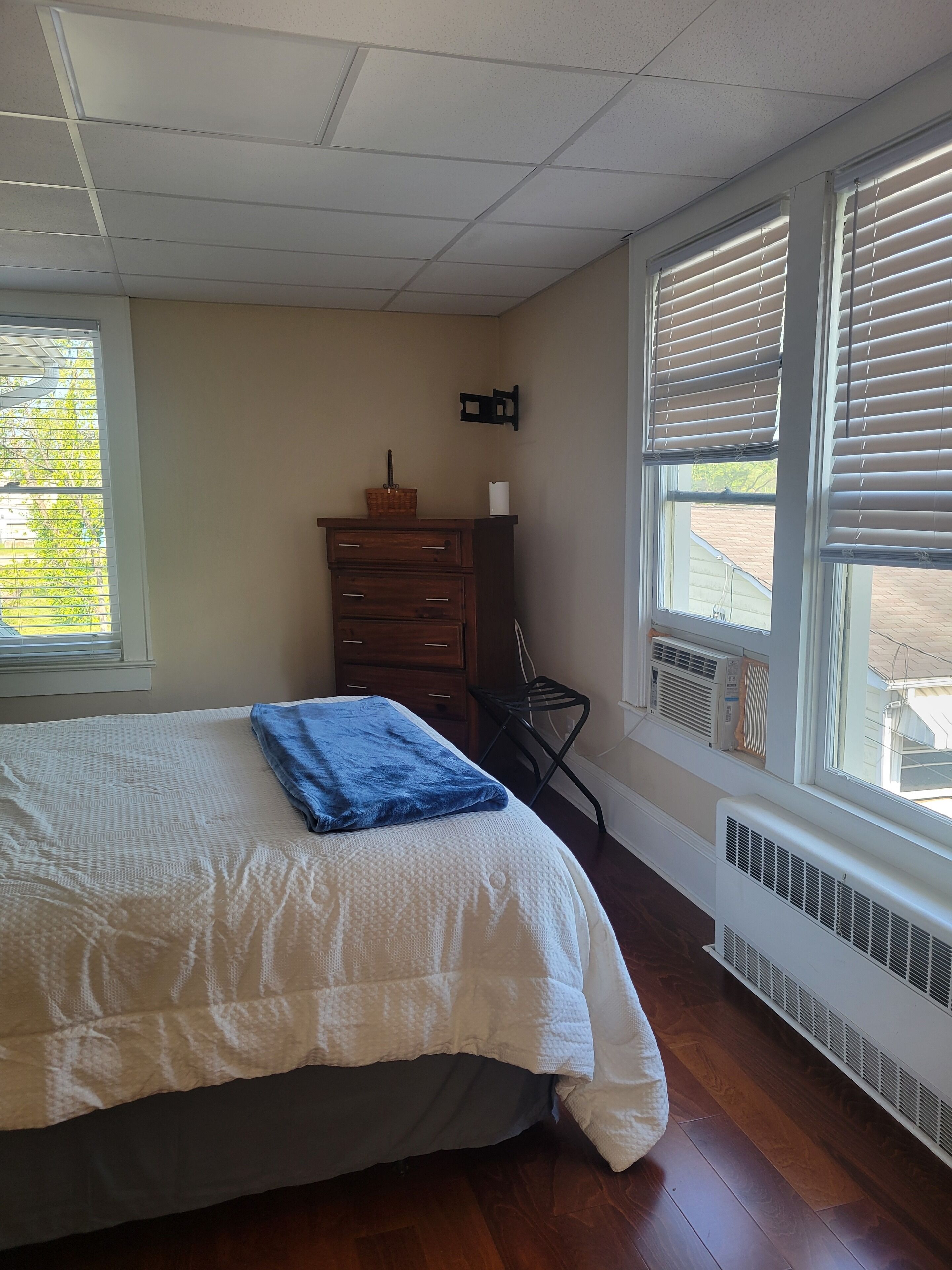 Una camera da letto con un letto, una cassettiera, un termosifone e una finestra con persiane.