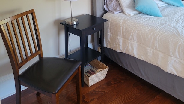 Een slaapkamer met een bed, een stoel, een nachtkastje, een lamp, een schilderij en een plank.
