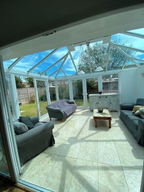 A conservatory with a glass roof, a grey sofa, a wooden coffee table, and a white cabinet. - Spacious beach bungalow, less than 5 minutes walk to the beach (Bognor Regis)