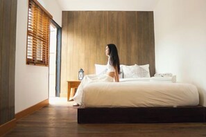 A bedroom with a wooden headboard, a bed with white bedding, a nightstand with a lantern, and a window with wooden blinds. - The Folkster House Chiangkhan (Chiang Khan)