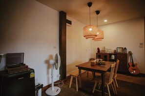 A dining area with a wooden table, chairs, a fan, a guitar, and a hanging light fixture. - The Folkster House Chiangkhan (Chiang Khan)