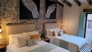 A room with two beds, stone walls, and artwork of wings. - Castello di Carlo – Loft Carlo VI (Val'Quirico)