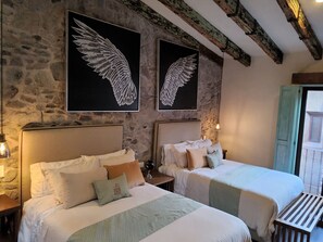 Habitación con dos camas, paredes de piedra y una obra de arte con alas.