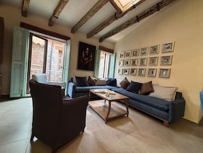Una sala de estar acogedora con sofá, sillón y mesa de centro. Hay varias fotos enmarcadas en la pared y un cuadro grande sobre el sofá.