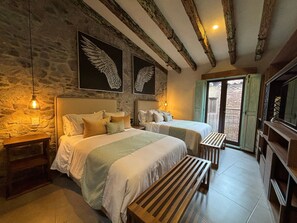 A bedroom with two beds, stone walls, wooden beams, a bench, and a TV. - Castello di Carlo – Loft Carlo VI (Val'Quirico)