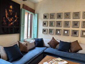 A living room with a blue sofa, multiple cushions, a large framed picture, and a collection of framed mirrors on the wall. - Castello di Carlo – Loft Carlo VI (Val'Quirico)