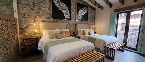 A bedroom with two beds, stone walls, wooden beams, and artwork of wings.