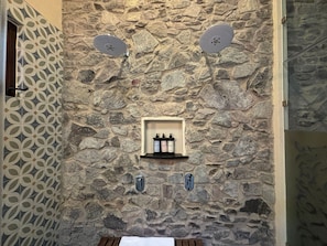 A stone wall with a shelf holding toiletries and two wall-mounted towel dispensers. - Castello di Carlo – Loft Carlo VI (Val'Quirico)