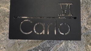 A black nameplate with the name 'Carlo' and a Roman numeral 'VIII' engraved on it. - Castello di Carlo – Loft Carlo VI (Val'Quirico)