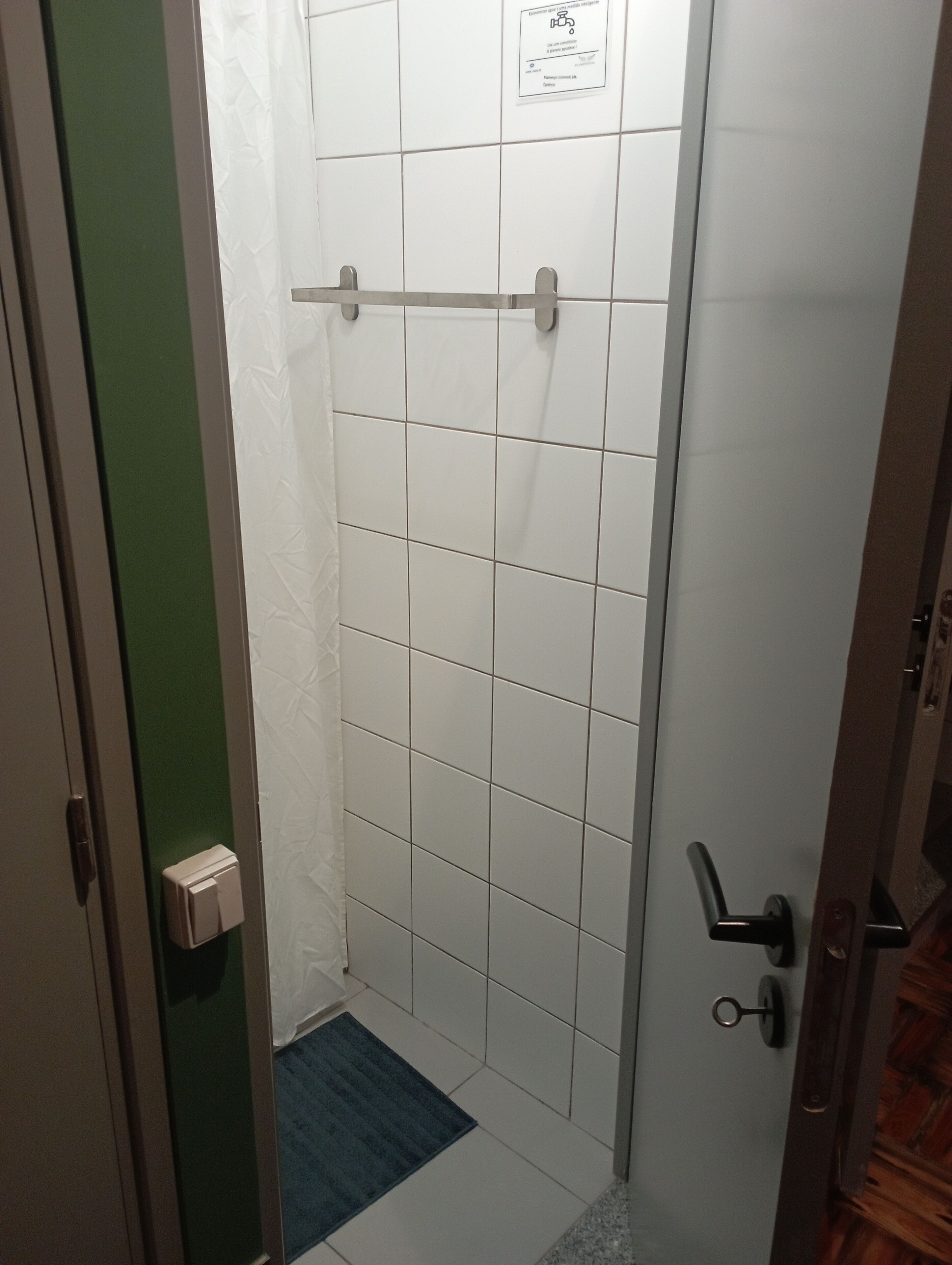 A bathroom with white tiles, a towel rack, a door with a handle, and a blue mat on the floor.