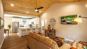 Ein geräumiger Wohnbereich mit Holzboden, einer Couch, einem Couchtisch und einem an der Wand montierten Fernseher.