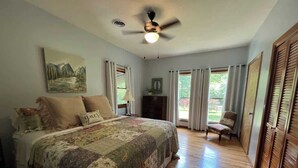 Quarto com cama grande, ventilador de teto e vista para o exterior pela janela.