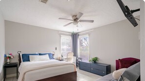 Un dormitorio con cama, escritorio, silla, ventilador de techo y ventana con persianas.