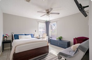 A bedroom with a bed, a desk, a chair, a ceiling fan, and a window with blinds.