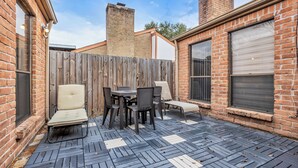 Un patio con pared de ladrillo, cerca de madera y una mesa con sillas.