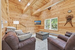A cozy cabin interior with wooden walls, a sofa, a coffee table, and a window with a view of trees. - New Built! 2025 Cozy 3-bedroom chalet with water access to Rangeley Lake (Rangeley)