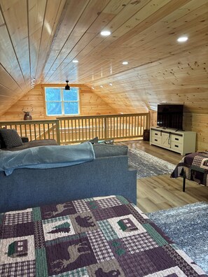 Quarto de sótão acolhedor com teto de madeira, uma janela grande, televisão e um sofá.