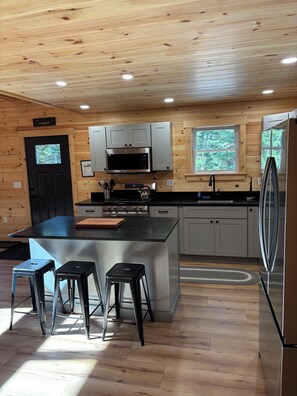A modern kitchen with a central island, stainless steel appliances, and wooden paneling.