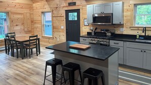 A wooden cabin interior with a kitchen featuring a stove, microwave, and bar stools.