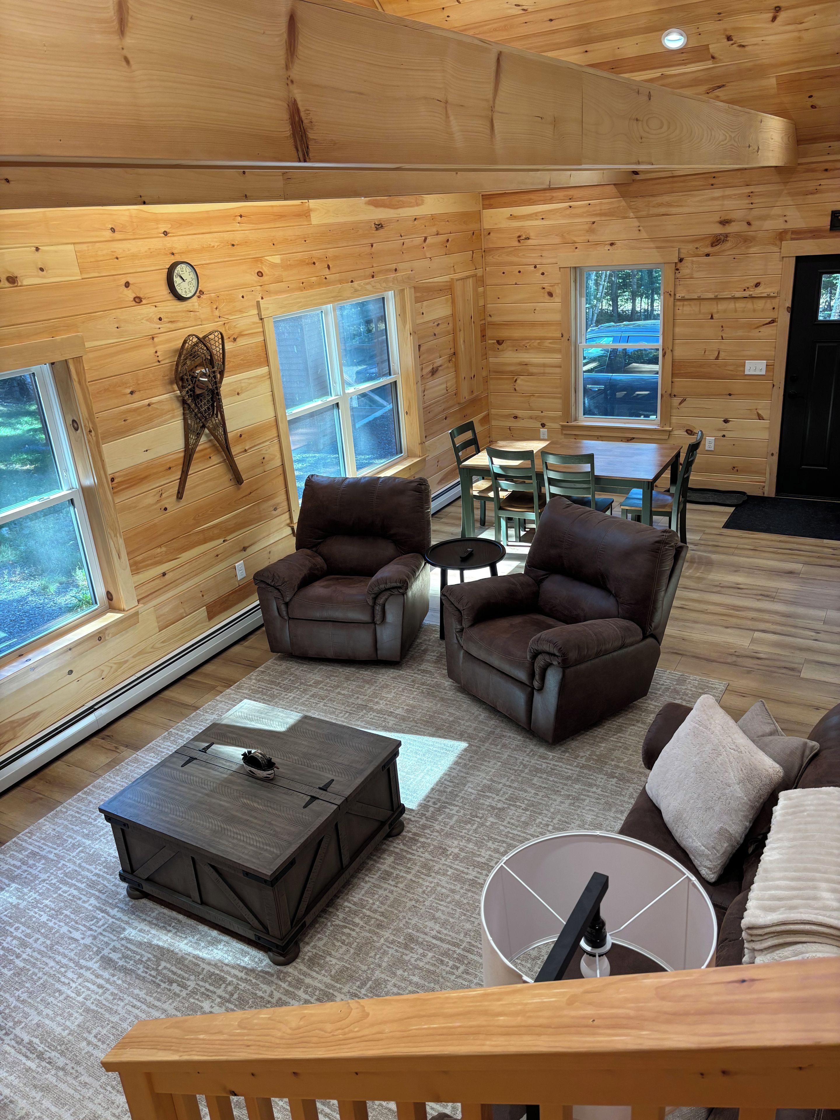 A cozy cabin interior with wooden walls, a dining table, two sofas, and a coffee table.