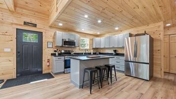 Una cocina moderna con paredes de madera, una isla central, taburetes de bar, electrodomésticos de acero inoxidable y una puerta negra.