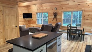 A wooden cabin interior with a kitchen, dining area, and seating.