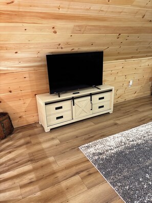A wooden wall with a television on a cabinet, a rug on the floor, and a basket on the left.