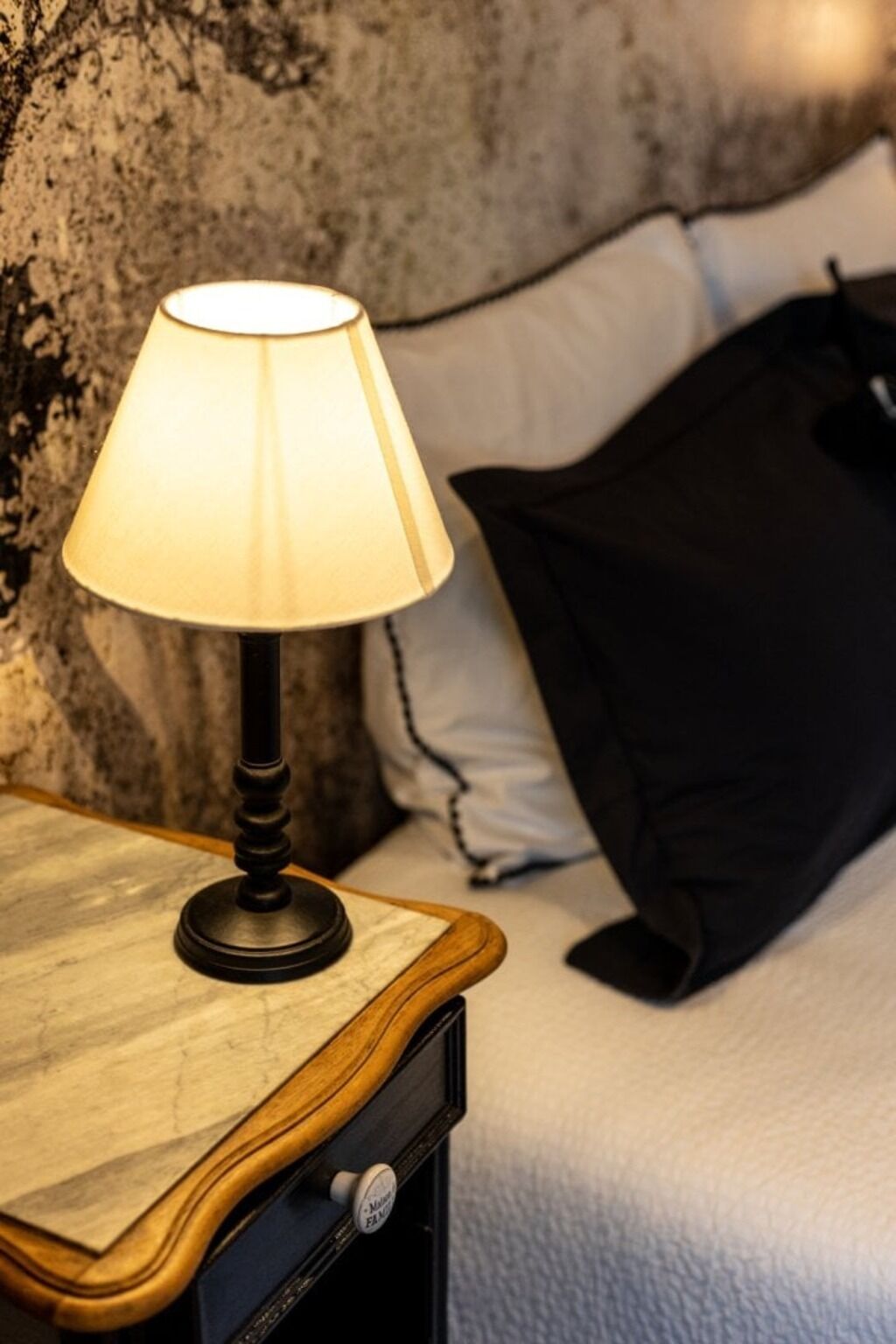 Une table de chevet avec une lampe, une commode en bois et un lit avec des oreillers.