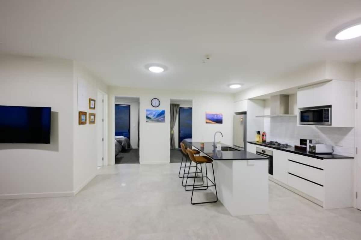 A modern kitchen with white cabinetry, a black countertop, and a built-in microwave. There are bar stools and a clock on the wall.