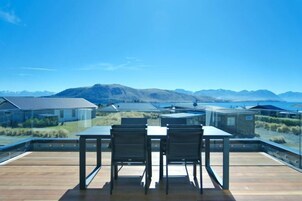 Terraza en la azotea con una mesa y sillas, con vistas a un paisaje montañoso y un cuerpo de agua.