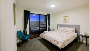 A hotel room with a bed, a chair, a nightstand, a lamp, and a view through a glass door. - Stargazing Tekapo Apartment (Lake Tekapo)