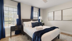 Un dormitorio con cama, mesitas de noche, ventilador de techo y ventana con cortinas.