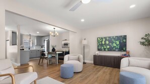 Una sala de estar moderna con comedor, una cocina al fondo y una gran obra de arte con hojas verdes en la pared.