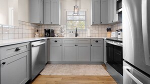 Una cocina moderna con gabinetes grises, un refrigerador de acero inoxidable y una ventana con persianas.