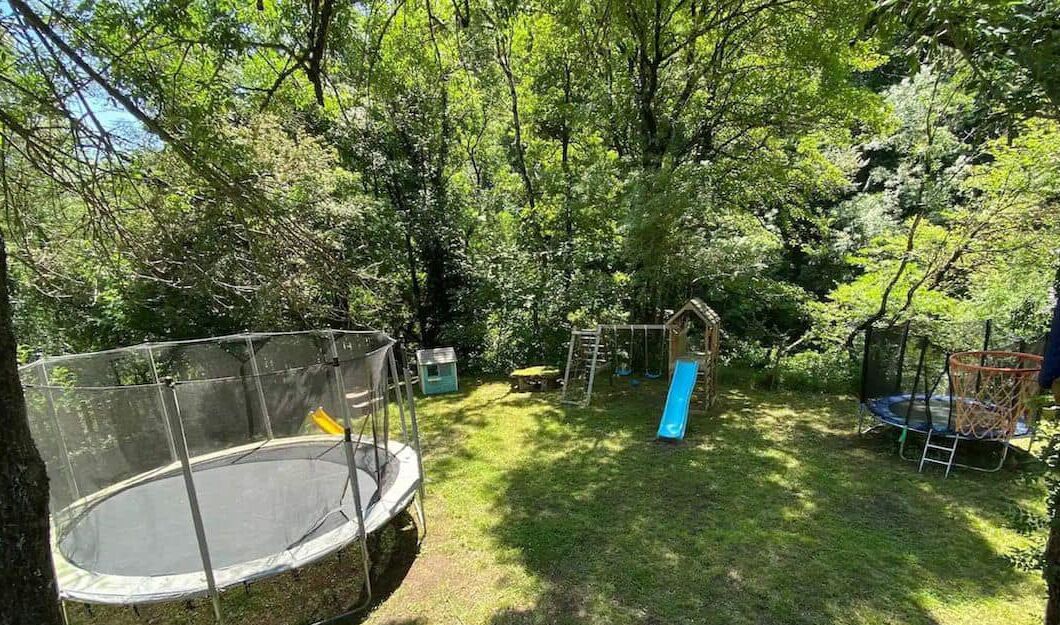 A playground with a trampoline, slide, and swing set surrounded by trees.
