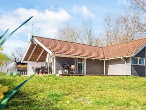 Una casa de un piso con techo inclinado, un porche cubierto y una parrilla.