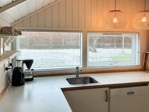 Una cocina con un lavamanos, una cafetera y un lavavajillas Bosch. Hay dos ventanas con persianas y se ve un ventilador de techo.