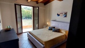 A bedroom with a bed, a nightstand, and a view of the outdoors through a sliding door. - Maya House. (La Ciaccia)