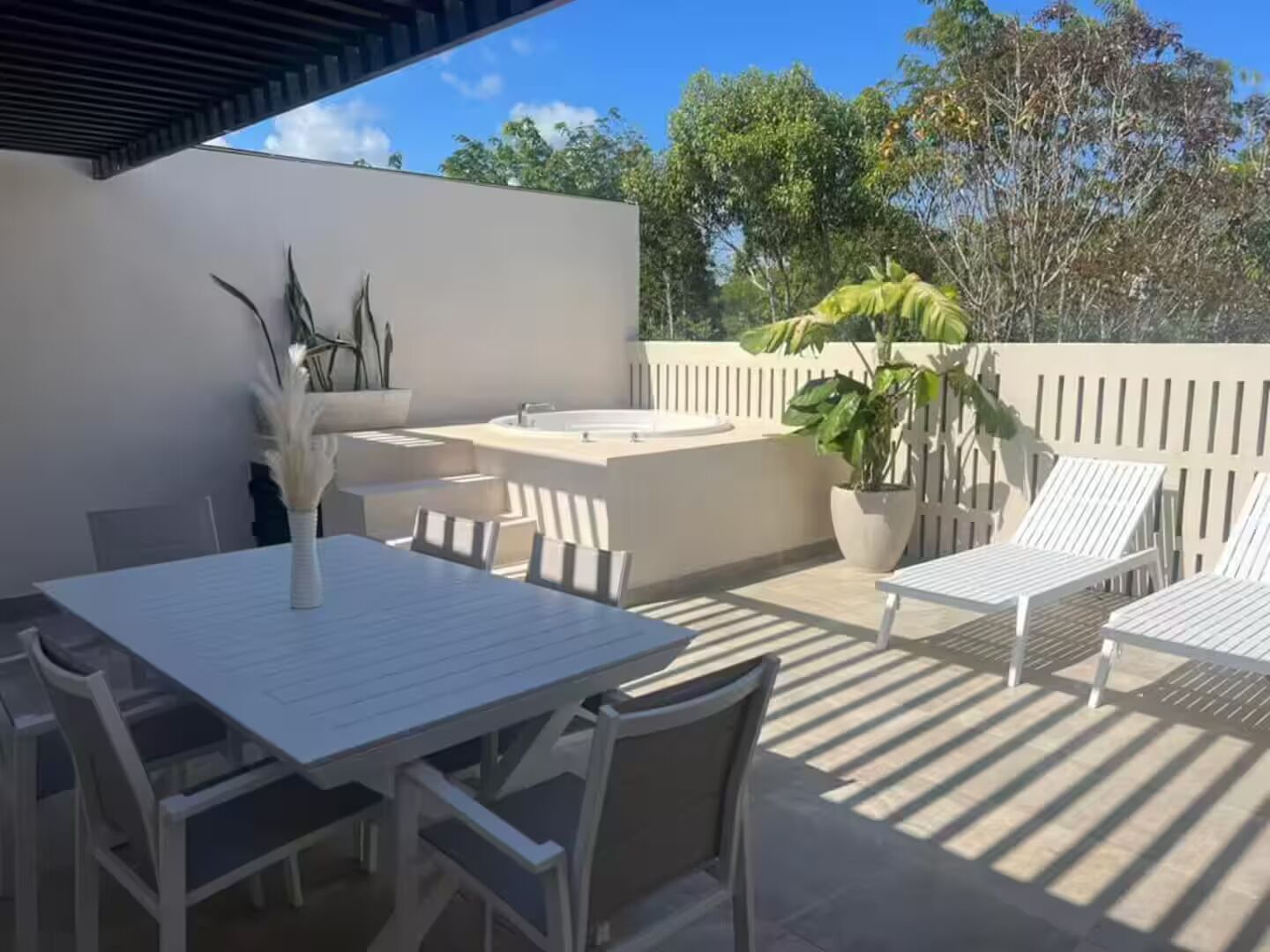Une terrasse avec une table et des chaises, un petit évier et une plante en pot.