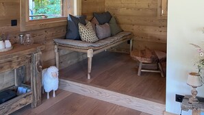 Ein gemütliches Blockhauss-Interieur mit einer Holzbank, einem kleinen Tisch und einem Fenster mit Blick ins Grüne.