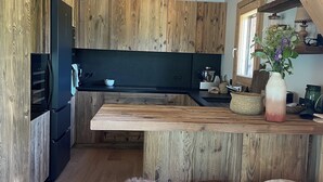 Eine moderne Küche mit Holzausstattung, einem schwarzen Kühlschrank, einer Holz Arbeitsplatte und drei Barhocker.