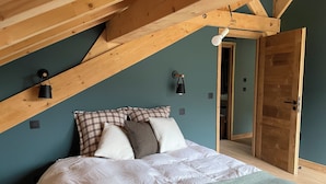 Ein Schlafzimmer mit Schrägdecke, einem Bett mit Karo- und Weißmuster, zwei Wandlampen und einer Holztür.