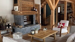 Ein gemütliches Wohnzimmer mit Kamin aus Stein, Holzbalken, einer Couch und einem Couchtisch.
