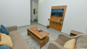 A modern living room with a wooden coffee table, beige sofa, and a TV mounted on a wooden panel. - أونيسن للشقق المخدومة Onsen Serviced Apartments (Al Kharj)
